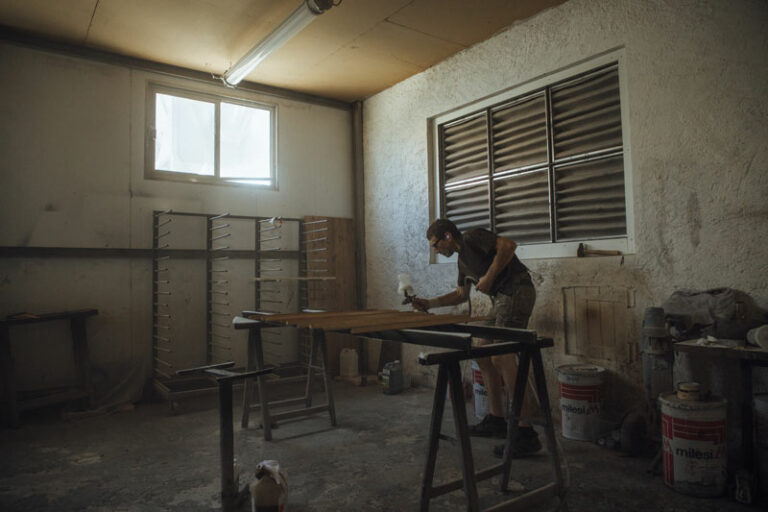 Un homme utilise du spray sur du bois, dans un atelier