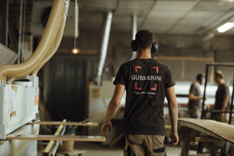 Un homme de dos, avec le logo Gusmerini dans le dos de son t-shirt, porte un casque anti-bruit