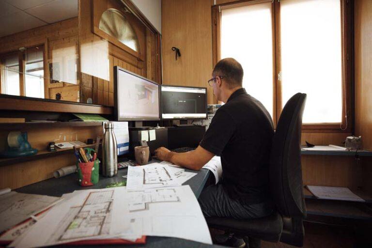Un homme à son bureau réalise des modélisations 3D avec des plans éparpillés sur son bureau